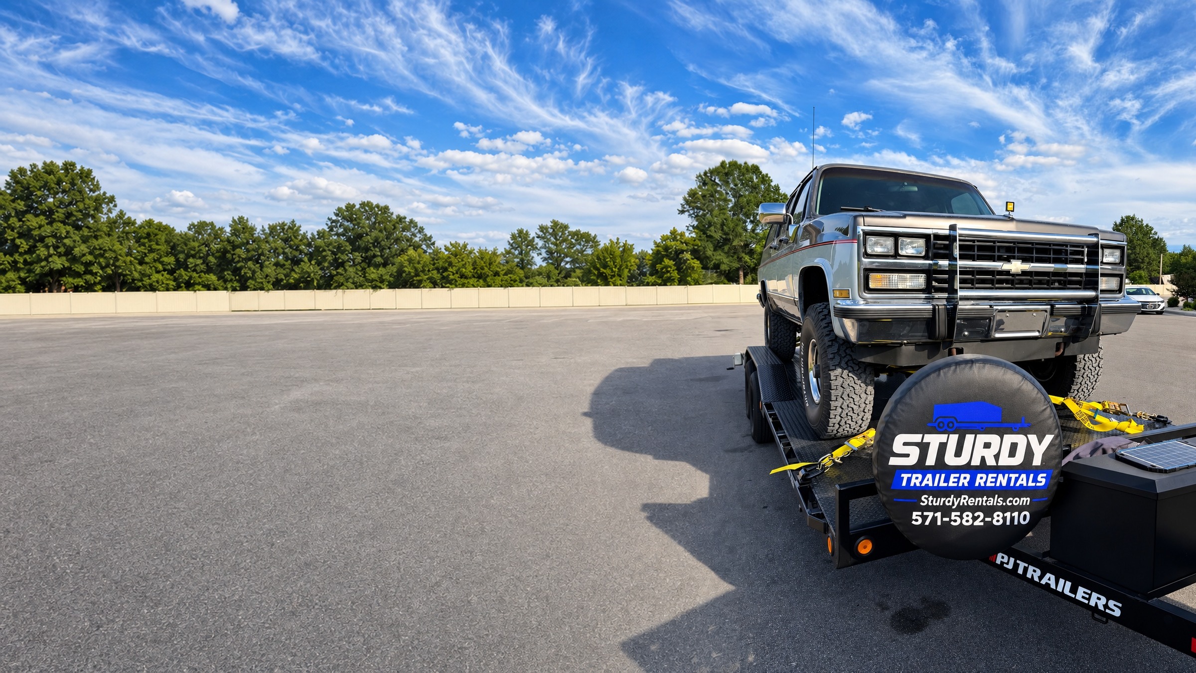 Classic Chevy Suburban loaded and strapped down on a Sturdy Rentals 20ft PJ car hauler trailer under a blue sky in Northern Virginia